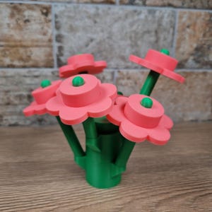May include: A bouquet of artificial flowers with pink petals and green stems and centers. The flowers are arranged in a green vase. The background is a brick wall and a wooden surface.