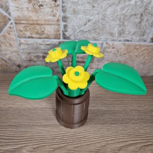 May include: A decorative flower arrangement featuring yellow flowers with green stems and leaves, set in a brown barrel-shaped pot. The flowers have a bright yellow center and petals. The leaves are a vibrant green.