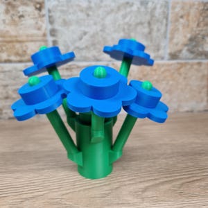 May include: A 3D-printed flower arrangement featuring five blue, multi-layered flower blooms with green centers. The stems and base are green, creating a vibrant contrast. The flowers are arranged in a bouquet style, suitable for home decor.