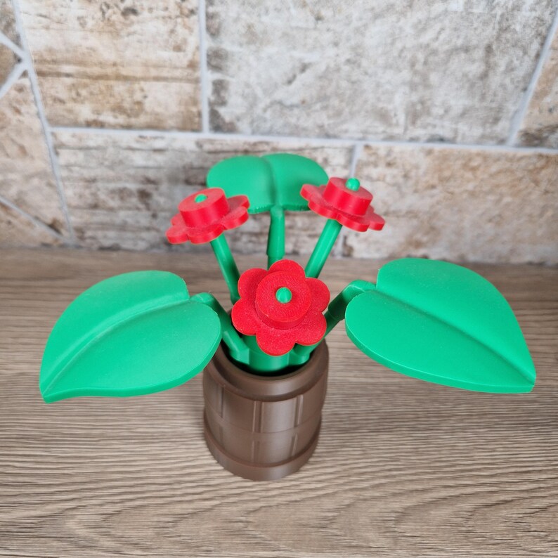 May include: A decorative, 3D-printed flower arrangement. The arrangement features three red flowers with green centers and leaves, set in a brown barrel-shaped pot. The leaves are a vibrant green, and the pot has a textured surface.