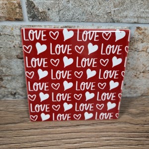 K&ouml;nnte beinhalten: Ein roter quadratischer Keramik-Blumentopf mit dem Wort "LOVE" und wei&szlig;en Herzformen. Der Topf ist mit dem Wort "LOVE" und wei&szlig;en Herzen verziert. Geeignet f&uuml;r den Innen- und Au&szlig;enbereich.