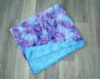 May include: A soft, plush blanket with a tie-dye pattern in shades of blue and purple. The blanket is folded in half, revealing a solid blue underside.