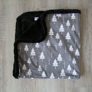 May include: A gray and white baby blanket with a pattern of white trees on a gray background. The blanket has a black minky backing.