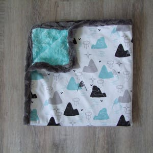 May include: A soft, plush baby blanket with a white background and a pattern of blue and gray mountains. One side of the blanket is a soft, plush fabric, while the other side is a smooth, cotton fabric.