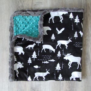 May include: A black and white baby blanket with a gray minky backing. The blanket features a woodland animal print with moose, deer, bears, and trees.