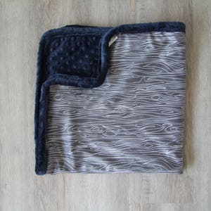 May include: A soft, gray and white baby blanket with a woodgrain pattern. The blanket has a navy blue minky backing.