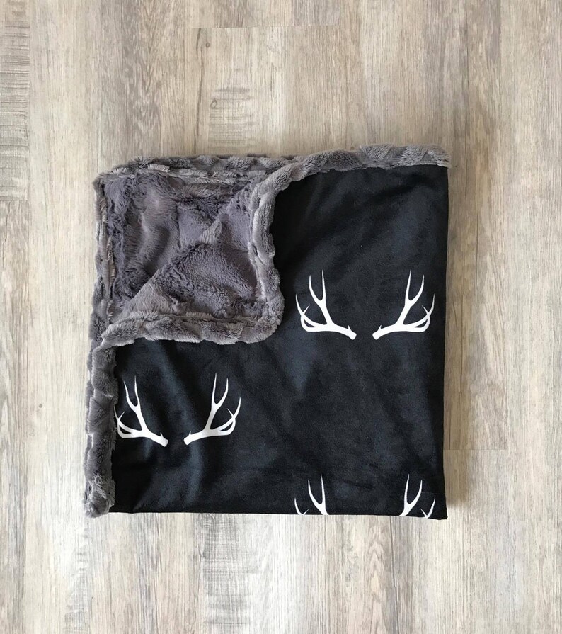 May include: A black and gray fleece blanket with a white deer antler pattern. The blanket is soft and cozy, perfect for snuggling up on the couch.
