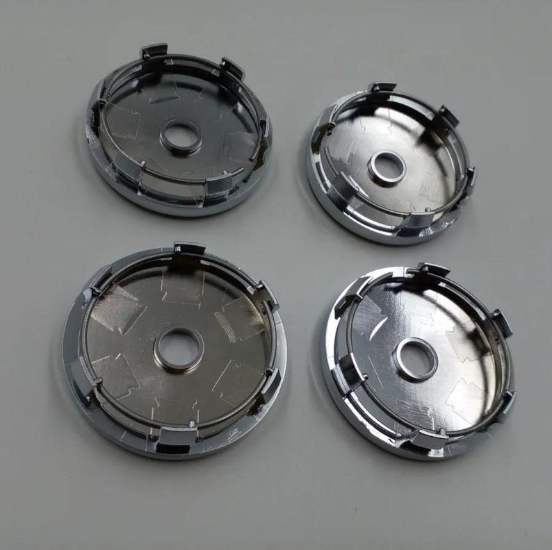 May include: Four chrome-finished hubcaps, each with a central circular opening and a series of securing clips around the perimeter. The hubcaps have a reflective surface, suggesting a polished metal finish. The arrangement is symmetrical.