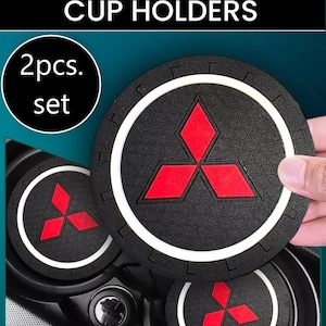 Może przedstawiać: Czarne uchwyty na kubki do wnętrza samochodu z czerwono-białym logo. Zestaw zawiera dwie sztuki. Tekst "CAR INTERIOR CUP HOLDERS" znajduje się na górze obrazu.