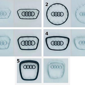 Può includere: Una collezione di design di emblemi per auto, con il logo Audi. Gli emblemi sono in varie forme, tra cui circolari e rettangolari, con cornici argentate e nere. Il logo Audi è composto da quattro anelli intrecciati.