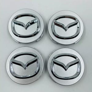 Puede incluir: Cuatro tapacubos Mazda plateados. Cada tapón presenta el logotipo de Mazda en acabado cromado, sobre un fondo plateado. Los tapones son redondos con un emblema pulido en relieve.