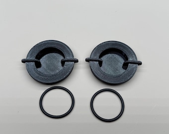 May include: Two black ashtrays with a circular design and a small notch for holding a cigarette. Two black rubber O-rings are also included. The ashtrays are made of a textured material.