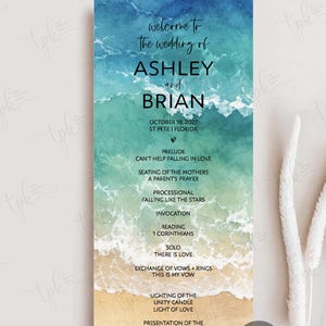 May include: A vertical wedding program card featuring a watercolor ocean wave design transitioning from deep blue to turquoise and sandy beige. The text includes the names Ashley and Brian, the date October 18, 2027, and a detailed ceremony order.