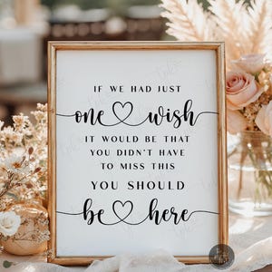 May include: A rectangular sign in a gold frame featuring black text on a white background that reads: IF WE HAD JUST one wish IT WOULD BE THAT YOU DIDN'T HAVE TO MISS THIS YOU SHOULD be here. The text includes two heart-shaped flourishes.