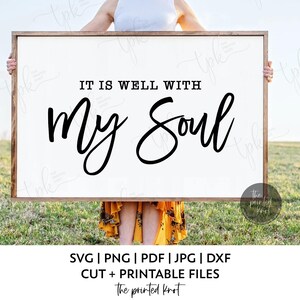 Könnte beinhalten: Ein gerahmtes weißes Schild mit dem Text "IT IS WELL WITH My Soul" in schwarzer Schrift. Das Schild wird von einer Person vor einem grasbewachsenen Feld gehalten. Der Rahmen ist hellbraun. Der untere Teil des Bildes enthält Informationen zum Dateityp.
