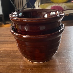 May include: Two brown ceramic bowls stacked on top of each other. The bowls have a glazed finish and a slightly rippled texture.