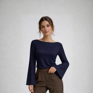 May include: A navy blue top with a boat neck and flared sleeves. The top is paired with brown trousers. The woman is standing in front of a white background.