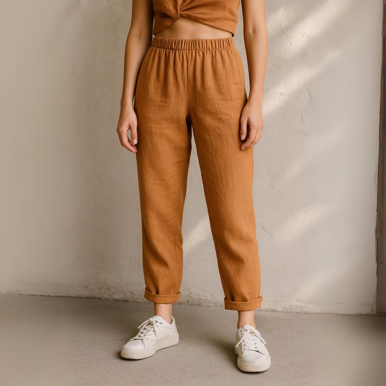 Puede incluir: Una persona con pantalones de lino marr&oacute;n con un top a juego y zapatillas blancas. Los pantalones tienen cintura el&aacute;stica y dobladillos con vuelta. El atuendo es informal y c&oacute;modo.