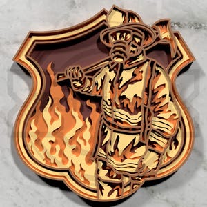 May include: A layered wooden art piece depicting a firefighter in uniform holding an axe, standing in front of flames. The artwork is in shades of brown, orange, and yellow, set against a shield-shaped background.