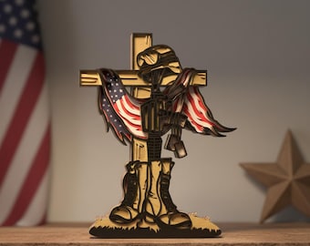 May include: A wooden memorial sculpture featuring a cross with a soldier's helmet, rifle, and boots. An American flag is draped over the cross. The sculpture is in shades of brown and gold, with red, white, and blue accents.