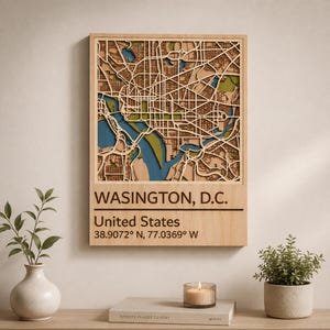 May include: A rectangular wooden wall art piece featuring a layered, laser-cut map of Washington, D.C. The map displays blue water features and green land areas. Below the map, the text reads WASINGTON, D.C., United States, 38.9072° N, 77.0369° W.