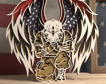 May include: A layered wooden sculpture of an eagle with outstretched wings, incorporating the American flag design. The eagle is depicted in a kneeling position, wearing a military uniform. The wings feature red and white stripes with blue and white stars.