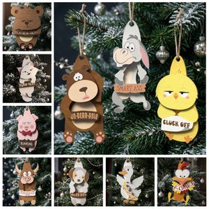 May include: A collection of wooden animal ornaments featuring a bear with UN-BEAR-ABLE, a cat with PURR-FECT, a pig with BOARING, a bull with UDDER-LY, a dog with RUFF DAY, a donkey with SMART ASS, a chick with CLUCK OFF, and a chicken with F-CAW-F.