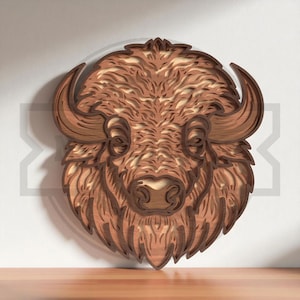 Puede incluir: Escultura de cabeza de bisonte de madera en capas. La obra de arte presenta un diseño detallado con diferentes tonos marrones, creando un efecto tridimensional. El bisonte tiene cuernos prominentes y una melena texturizada, adecuada para la decoración rústica.