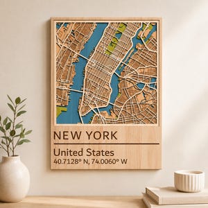 May include: A rectangular wooden wall art piece featuring a layered 3D map of New York City. The map displays blue water, light green parks, and tan urban areas. Below the map, the text reads: NEW YORK, United States, 40.7128° N, 74.0060° W.