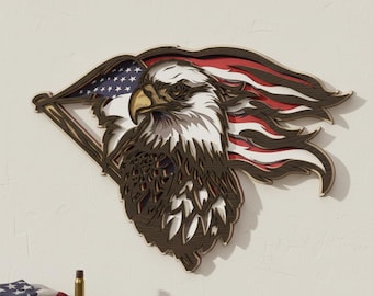 Op de afbeelding: Een gelaagd houten wandkunstwerk met een adelaar die een Amerikaanse vlag vasthoudt. De adelaar is afgebeeld met gedetailleerde veren en een gerichte blik. De vlag heeft rode en witte strepen en blauwe sterren. Het kunstwerk is op een witte muur gemonteerd.