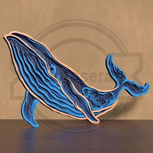 May include: A layered wooden whale sculpture in shades of blue and a light brown edge. The whale is depicted in a side profile, with detailed lines representing its form. The artwork is set against a neutral background.