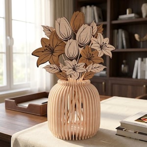 Könnte beinhalten: Eine Holzvase mit hellbraunem Finish hält einen Strauß Holzblumen. Die Blumen umfassen Lilien, Tulpen und Blätter, alle in Brauntönen. Die Vase hat ein vertikales Lamellendesign. Die Anordnung steht auf einem Tisch.