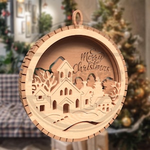 以下が含まれることがあります： 丸い木製のクリスマスオーナメント。教会のデザイン、木、そして「Merry Christmas」の文字が木にカットされています。自然な木の色で、吊り下げ用のループが付いています。