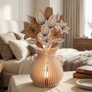 Könnte beinhalten: Eine holzgeschnitzte Vasenlampe mit Blumenarrangement. Die Lampe hat eine hellfarbene, vertikal geriffelte Vase mit warmem Schein von innen. Das Blumenarrangement umfasst Tulpen, Lilien und Blätter in Braun- und Beigetönen.