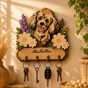 Könnte beinhalten: Schlüsselhalter aus Holz mit einem Hundedesign, Blumen und dem Text "Bless This Home". Der Schlüsselhalter hat vier Haken mit Schlüsseln, die daran hängen. Der Hund ist hellbraun mit einem lächelnden Gesichtsausdruck.