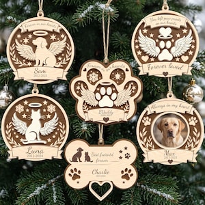 May include: Six wooden pet memorial ornaments with laser-cut designs. Features include angel wings, halos, paw prints, and engraved text such as 'Forever in our hearts', 'Sam', 'Buddy', 'Luna', 'Max', and 'Charlie' with dates and pet photos.