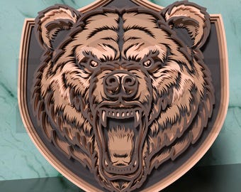 May include: A layered wooden bear head sculpture with an open mouth, revealing teeth. The bear is brown and tan, mounted on a shield-shaped frame with a dark gray background and a light brown border. The artwork is detailed and three-dimensional.