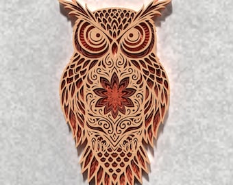 May include: A layered wooden owl wall art piece. The owl features intricate cut-out designs in shades of brown and reddish-brown. The owl's body has a floral design in the center. The owl has large eyes and pointed ear tufts.