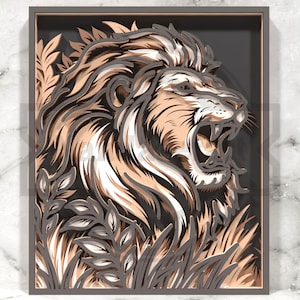 Puede incluir: Una obra de arte en papel en capas que representa a un león rugiendo con una melena detallada en tonos beige, blanco y marrón. El león está rodeado de follaje estilizado en gris y beige, todo dentro de un marco gris oscuro.