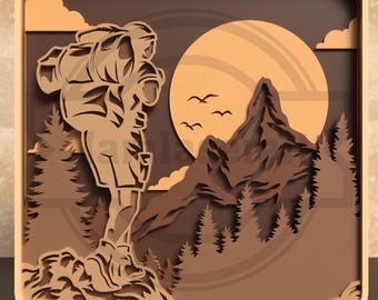 Puede incluir: Una obra de arte de madera en capas que representa a un excursionista con una mochila, montañas, árboles, un sol y pájaros. La obra de arte está en tonos marrones y beige, con un marco cuadrado.