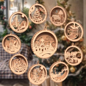 May include: A collection of nine wooden Christmas ornaments with various winter scenes. Each ornament is circular, with a detailed cutout design of a landscape, tree, or building. The ornaments are made of light-colored wood and have a loop for hanging.