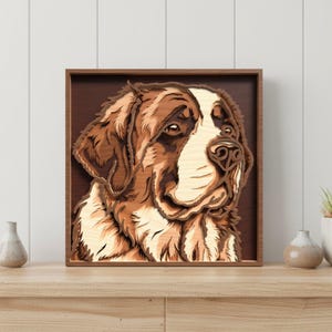 May include: A layered wooden artwork of a Saint Bernard dog's head, framed in a dark brown wooden frame. The dog's fur is depicted in shades of brown and cream, with detailed wood grain patterns. The artwork is displayed on a light wooden surface.