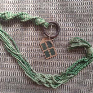 May include: A green macrame plant hanger with a wooden ring and a tassel. The hanger is made of cotton cord and has a gradient of green colours.
