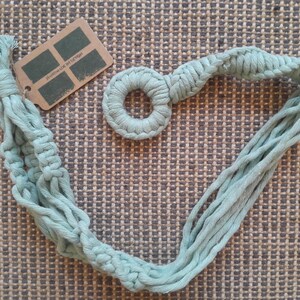 May include: A light blue macrame plant hanger with a circular ring at the top. The hanger is made of cotton cord and has a fringed edge.