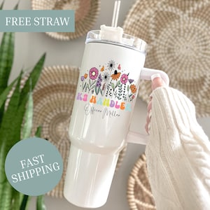 May include: White tumbler with a floral design and the text "KS Handler Officer Miller." The tumbler has a handle and a straw. The floral design includes pink, orange, and purple flowers.