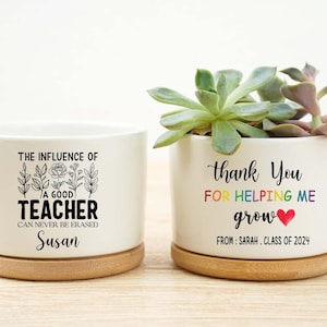 May include: Two white ceramic planters with wooden bases. One planter reads "The influence of a good teacher can never be erased" with the name "Susan". The other says "Thank you for helping me grow" with a heart and "From: Sarah, Class of 2024".