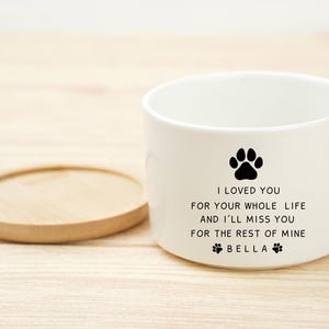 May include: White ceramic pet bowl with a black paw print and the text "I LOVED YOU FOR YOUR WHOLE LIFE AND I'LL MISS YOU FOR THE REST OF MINE BELLA". A wooden coaster is next to the bowl.