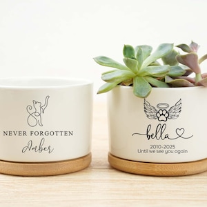 May include: Two white ceramic planters with bamboo bases. One features a cat silhouette and the text "NEVER FORGOTTEN Amber". The other has a paw print with wings and the name "Bella" with dates and the phrase "Until we see you again".