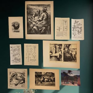 May include: A collection of vintage prints and illustrations displayed on a teal wall above a white marble cabinet with gold legs and handles. The prints depict various scenes, including botanical studies and historical figures.