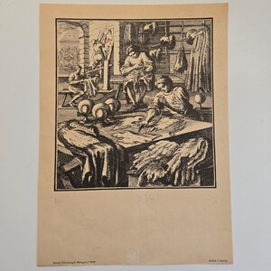 May include: A black and white print depicting a workshop scene with multiple figures. The print shows people working at tables, with barrels and hanging items in the background. The print is on a beige paper.